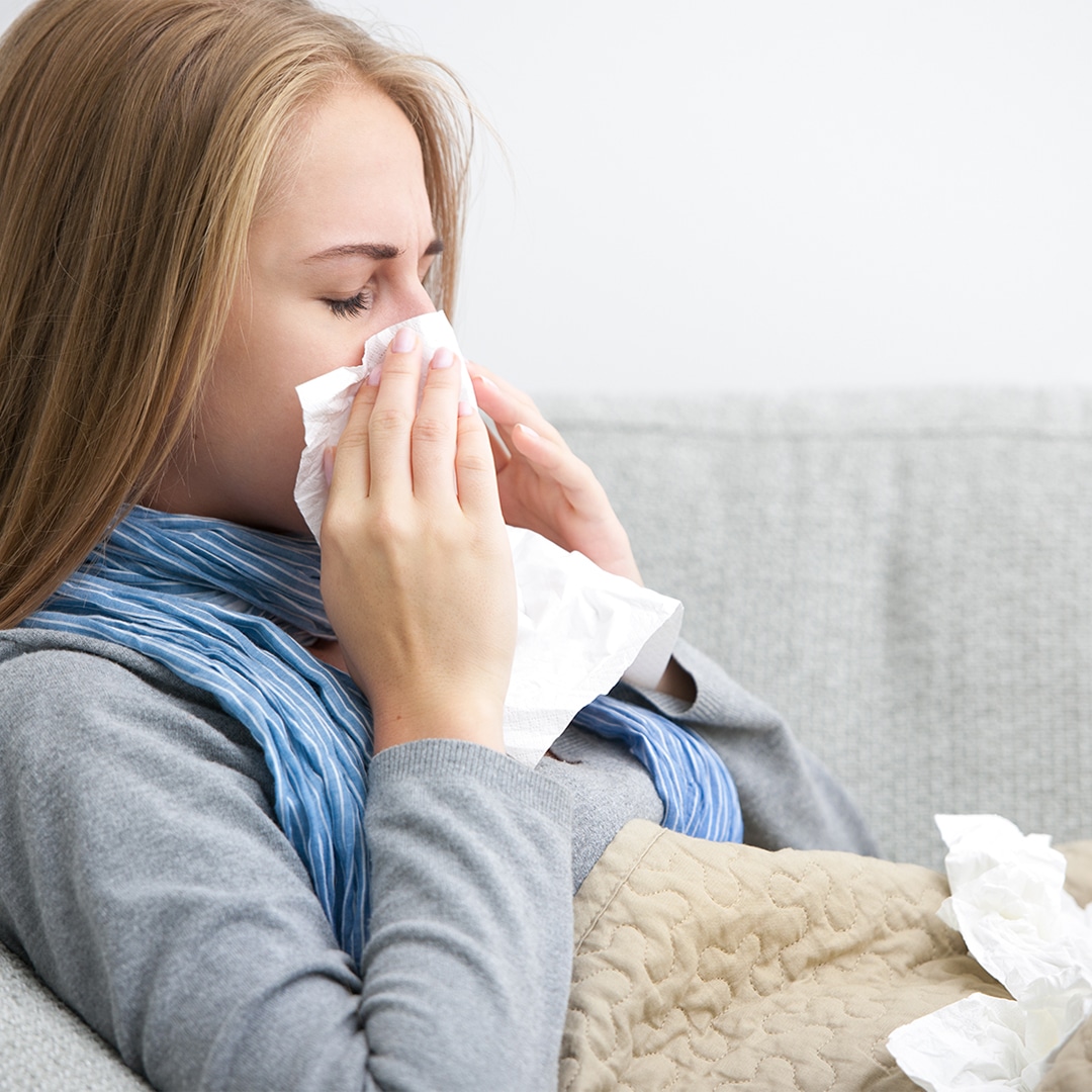woman sick on couch, blowing her nose