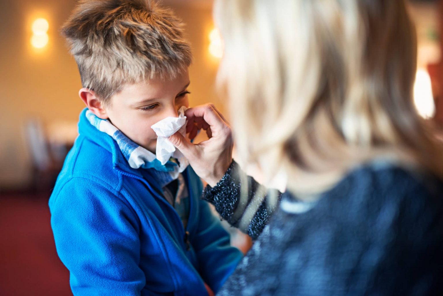 A young boy experiencing allergies blows his nose into a tissue.