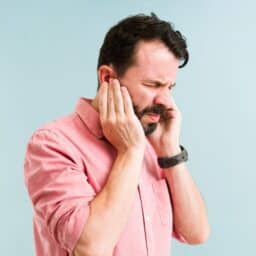 Man plugging both of his ears looking like he's in pain.