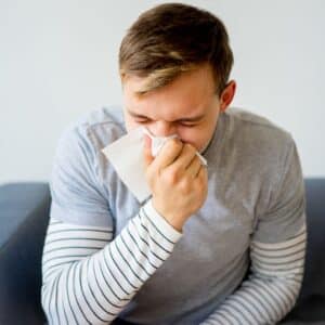 Man blowing nose, experiencing tonsilitis symptoms.