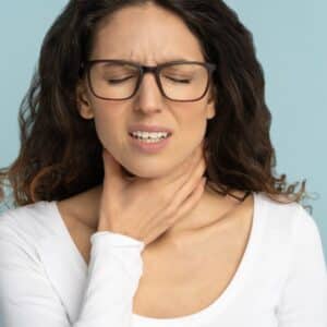 Woman with hand on throat experiencing tonsilitis.