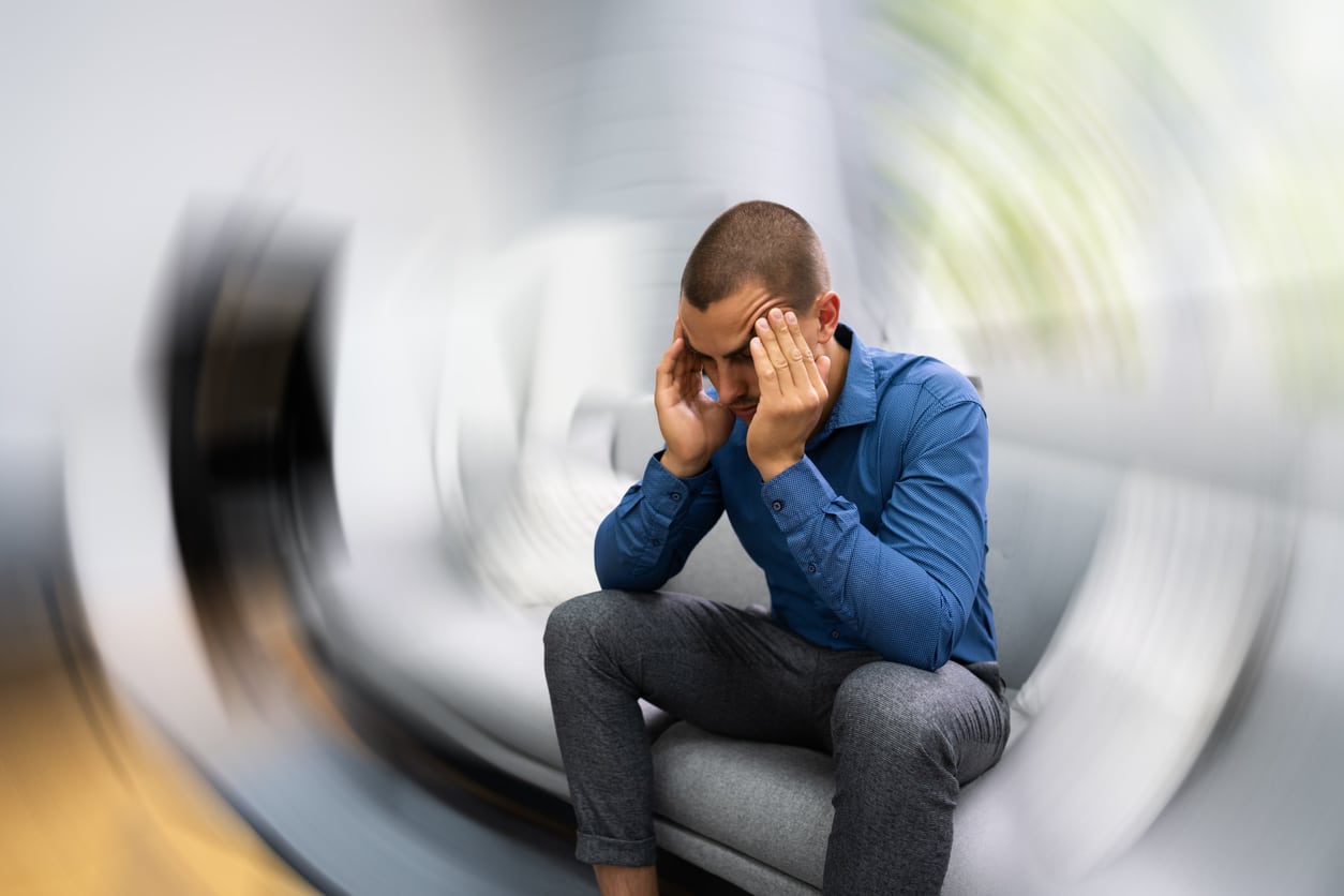 Man with vertigo sitting on the couch, head spinning.