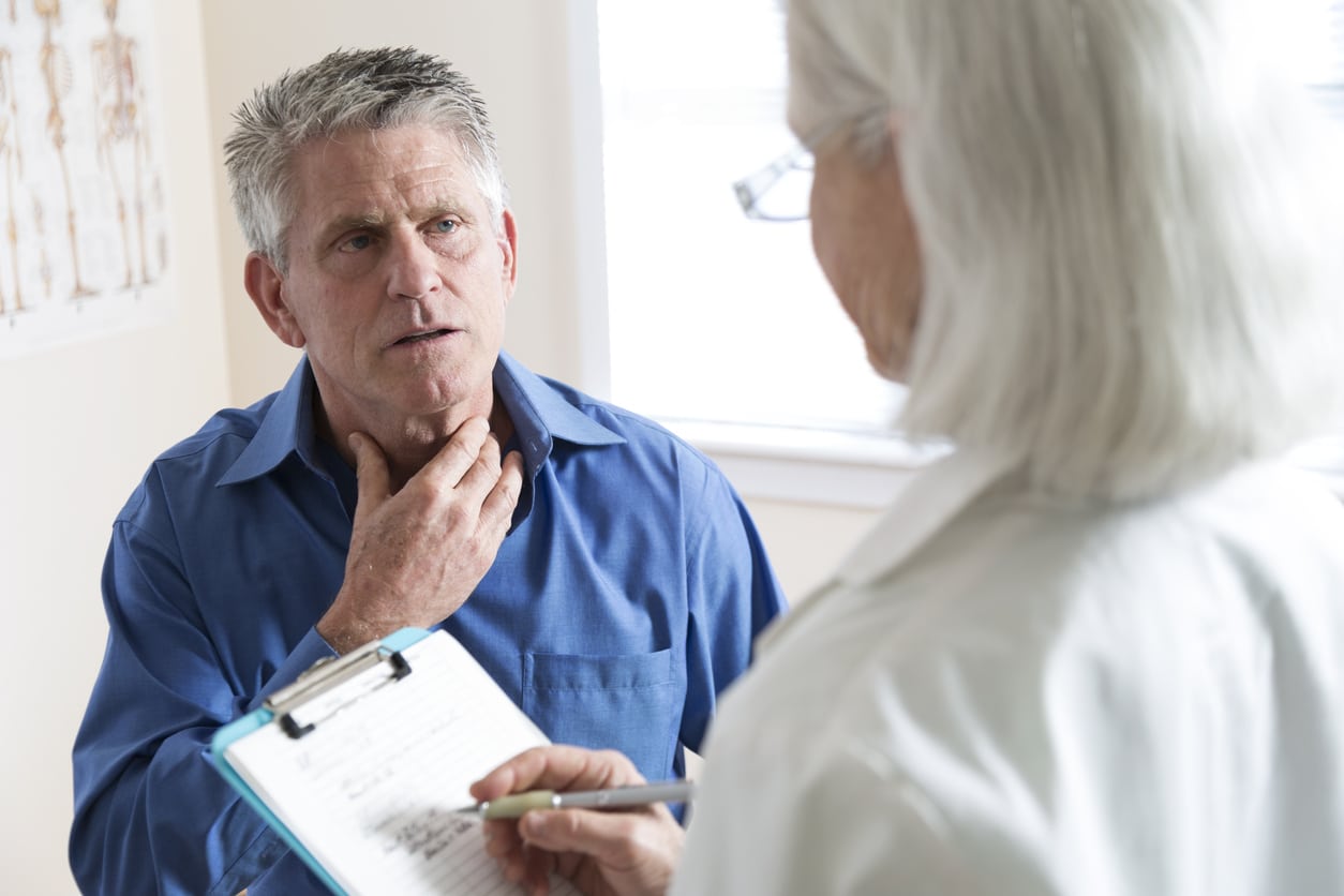 Senior man with a sore throat talking to his doctor.