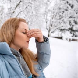 Woman with a sinus infection holding her nose, standing in the snow