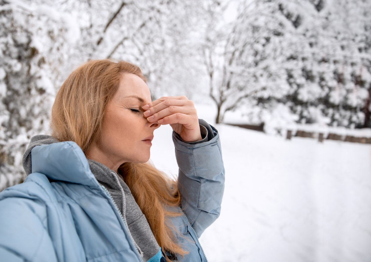 Woman with a sinus infection holding her nose, standing in the snow.