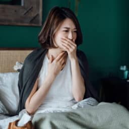 Woman holding her sore throat and coughing in bed