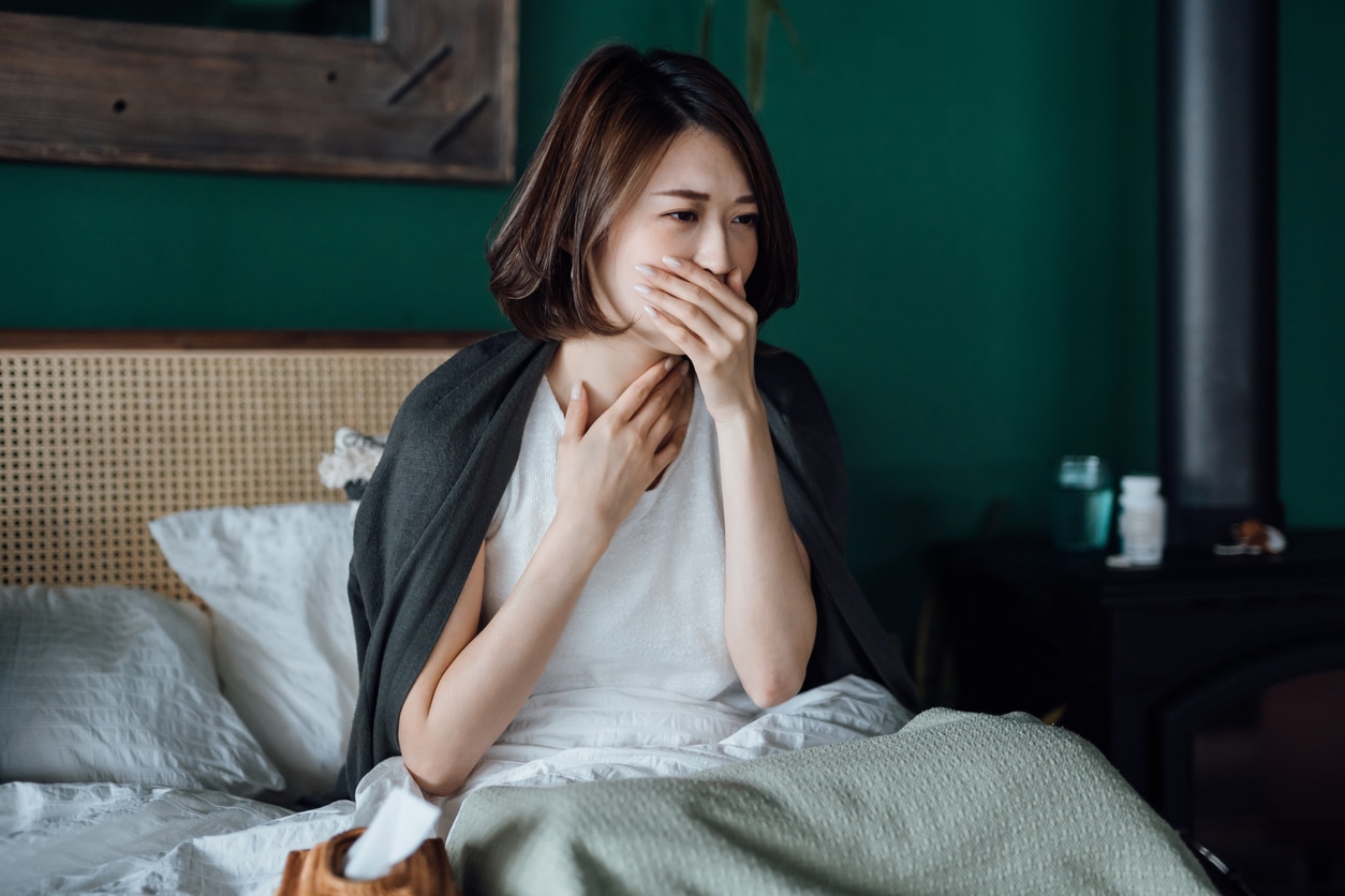 Woman holding her sore throat and coughing in bed.