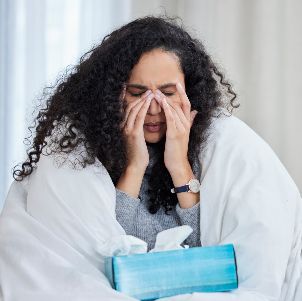 Woman wrapped in a blanket holding her sinuses.